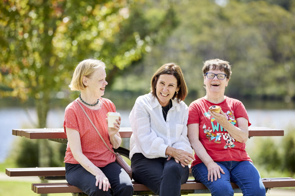 Sylvanvale site manager sits with two of the people she supports in park.